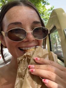 A woman wearing sunglasses enjoys a pastry while sitting outdoors. 